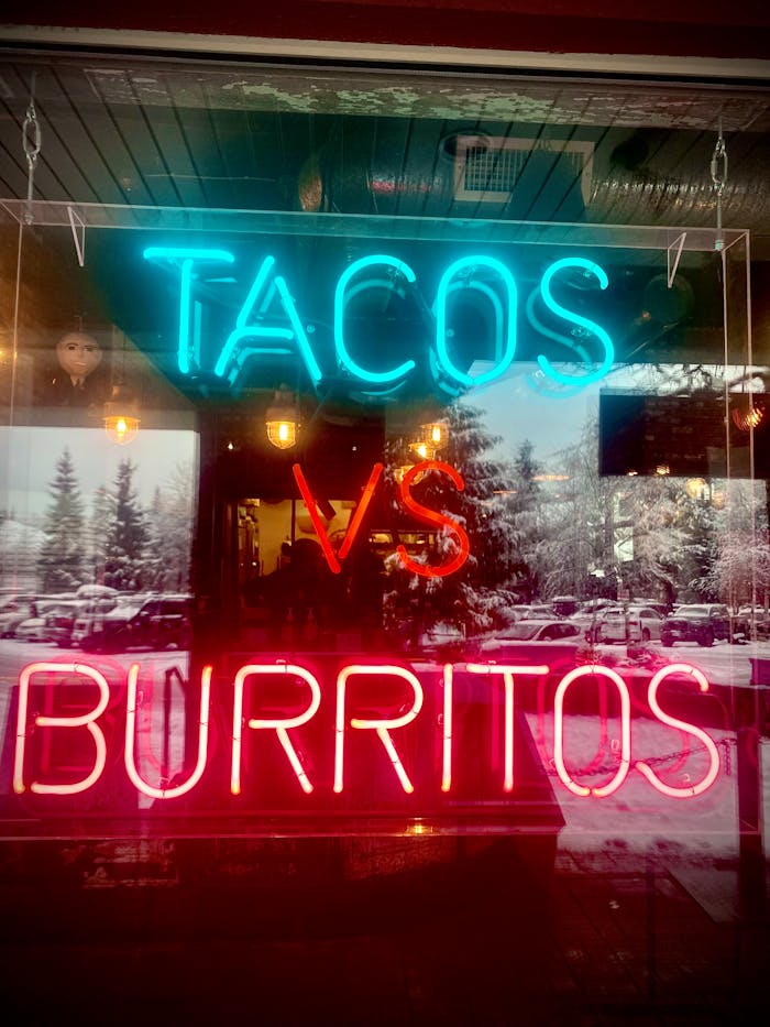 pexels-photo-10372506 Eye-catching neon sign highlighting tacos vs burritos debate in a shop window with snowy reflections.